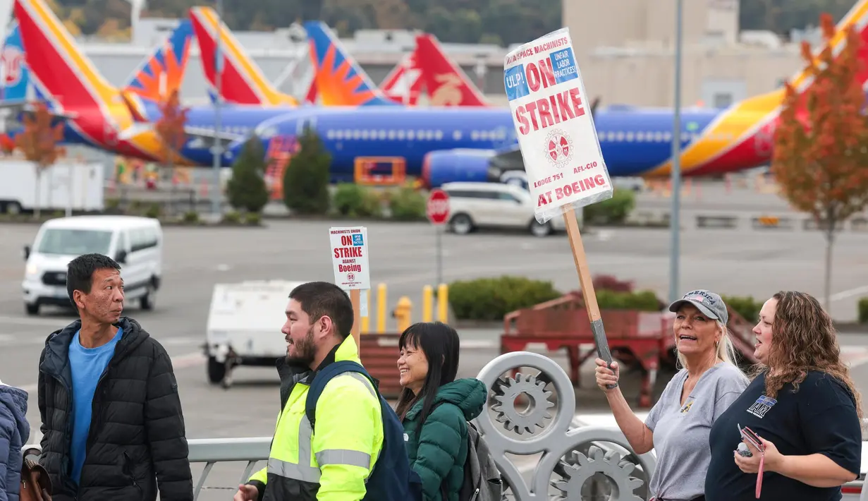 Orang-orang membawa tanda-tanda pemogokan Boeing saat mereka berjalan melewati pesawat Boeing 737 yang diparkir di dekat Boeing Field setelah aksi mogok kerja untuk Asosiasi Mekanik dan Pekerja Kedirgantaraan Internasional (IAM) di Seattle Union Hall di Seattle, Washington, pada tanggal 15 Oktober 2024. (Jason Redmond/AFP)