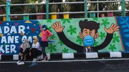 Warga berpose dengan mural yang mengajak orang untuk memakai masker di tengah pandemi Covid-19 di Surabaya, Jawa Timur, Minggu (25/10/2020). Mural di sepanjang dinding itu sebagai sarana imbauan kepada masyarakat untuk menerapkan protokol kesehatan pencegahan penularan COVID-19. (Juni Kriswanto/AFP)