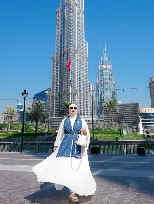 Berpose dengan latar gedung tertinggi di dunia, Burj Khalifa, Tasyi tampil glamor dengan dress putih yang dipadu syal LV warna biru dengan aksen chain belt, dan tas lady Dior warna senada dengan dress-nya. @tasyiiathasyia.