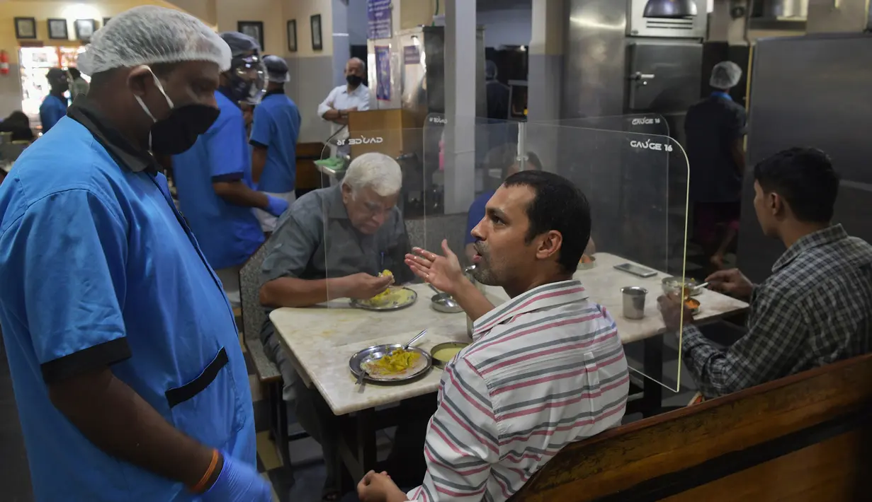 Pelanggan berbincang dengan pramusaji di sebuah restoran yang dibuka kembali usai pelonggaran lockdown di Bangalore, India, Senin (8/6/2020). Untuk keamanan pelanggan, restoran-restoran menyiapkan panel transparan di meja makan sebagai bagian dari rangkaian pencegahan COVID-19. (Manjunath Kiran/AFP)
