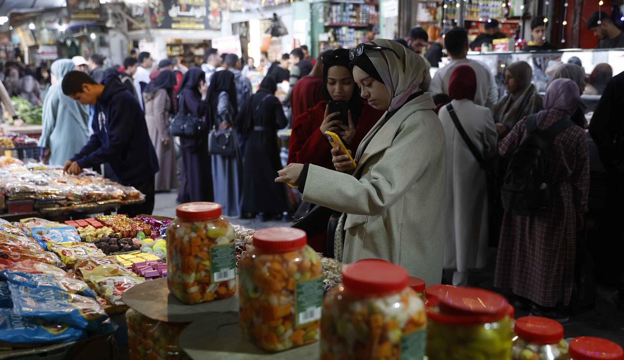 Kesulitan ekonomi membuat banyak warga Palestina di Kota Gaza harus lebih cermat dalam berbelanja kebutuhan Ramadan. Tampak dalam foto, para wanita Palestina berdiri di depan sebuah kios yang menjual manisan di pasar Zawiya, Kota Gaza, pada Rabu 18 Februari 2026. (Omar AL-QATTAA/AFP)
