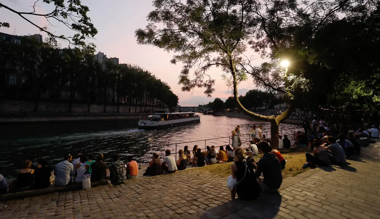Orang-orang duduk saat sore hari di tepi sungai Seine sebagai bagian dari acara musim panas Paris Plages di Paris, Prancis (7/7). (AFP Photo/Francois Guillot)