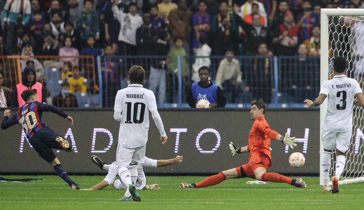Pemain Barcelona, Gavi (kiri) berhasil mencetak gol pertama ke gawang Real Madrid yang dijaga Thibaut Courtois dalam pertandingan Supercopa de Espana di King Fahd Stadium, Arab Saudi, Senin (16/1/2023) WIB. (AFP/Guiseppe Cacace)