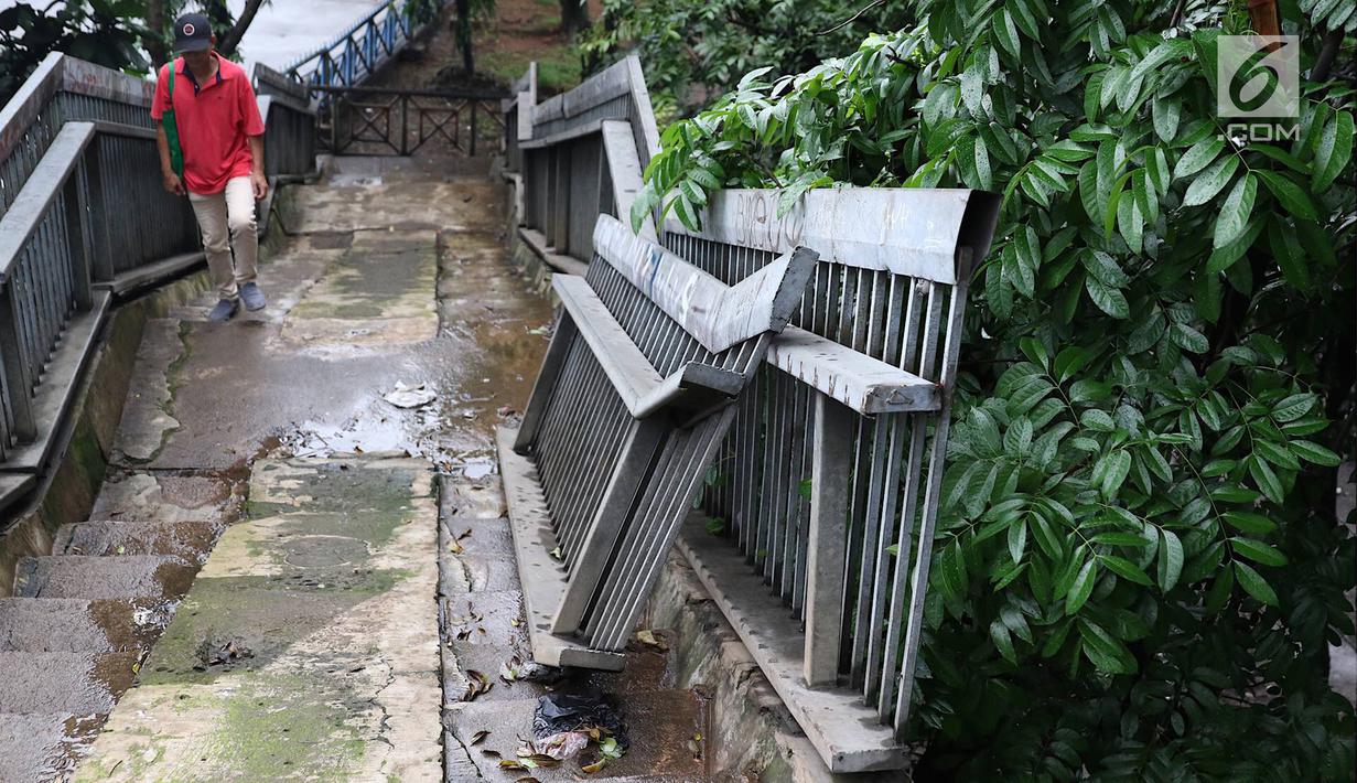 Pejalan kaki menaiki tangga JPO yang rusak di Terminal Kampung Rambutan, Jakarta, Senin (28/1). Kondisi JPO yang sebagian pagar pembatasnya rusak tersebut membahayakan pejalan kaki apabila tidak segera diperbaiki. (Liputan6.com/Immanuel Antonius)