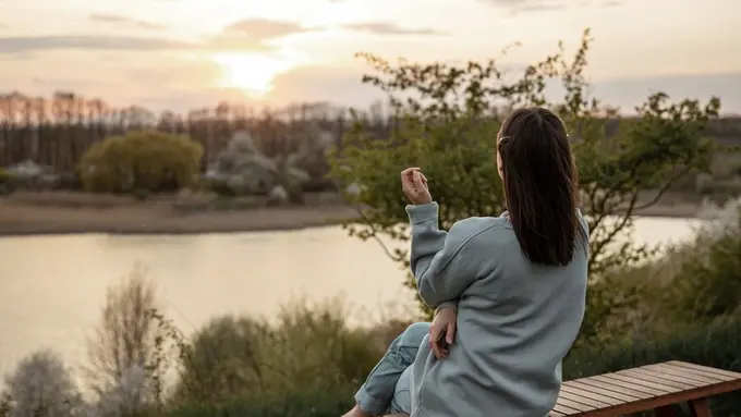 Seorang perempuan sedang menikmati senja di tepi sebuah danau (Foto Dok: Freepik/pvproductions)