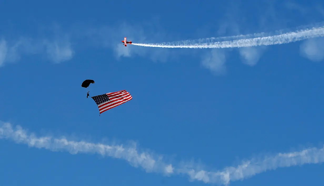 Seorang penerjun payung mengibarkan bendera negara Amerika Serikat saat beraksi di Brunswick, Maine (26/8). (AP Photo / Robert F. Bukaty)