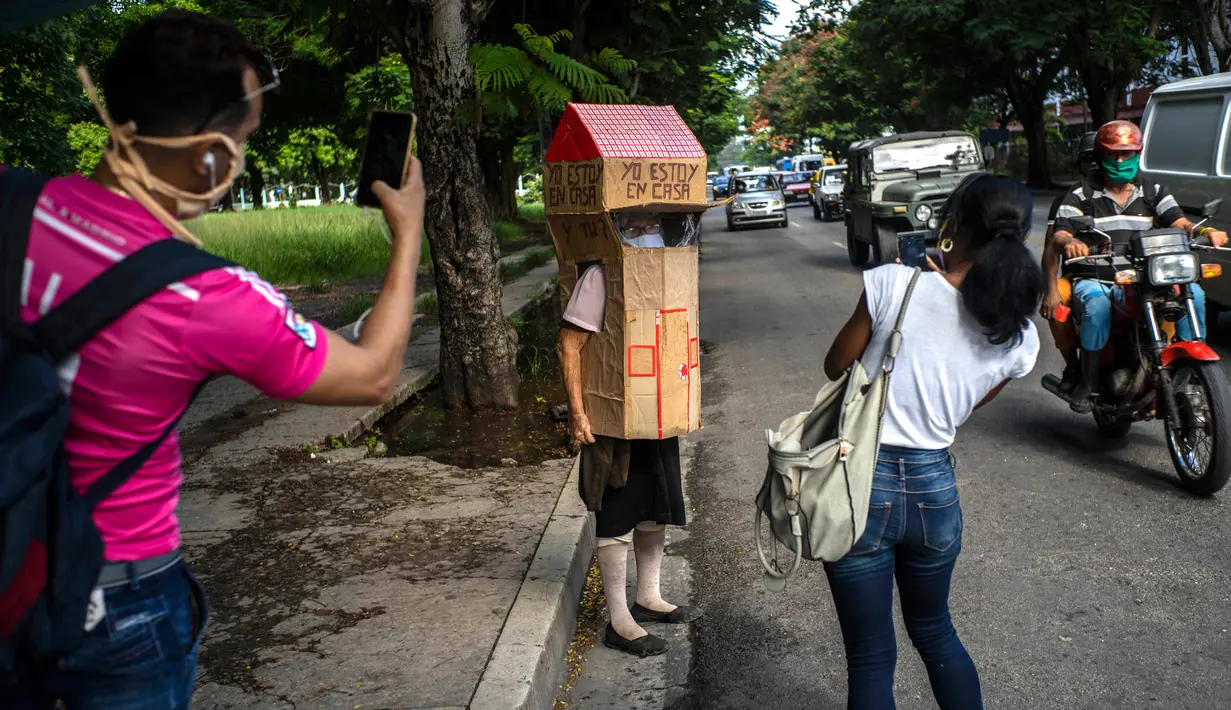 Orang-orang mengambil gambar pensiunan perawat, Feridia Rojas yang memakai kotak kardus berbentuk rumah untuk melindungi dirinya dari penyebaran Covid-19 di Havana, Kuba, 8 Juli 2020. Pakaian pelindung kardus itu dipakai Rojas untuk melakukan aktivitas di luar rumah sehari-hari. (AP/Ramon Espinosa)