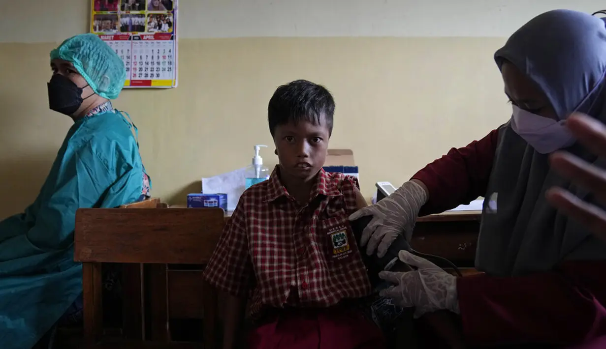 Seorang petugas medis memeriksa kondisi kesehatan seorang siswa sebelum disuntik vaksin COVID-19 pada kampanye vaksinasi di sebuah sekolah untuk anak-anak berkebutuhan khusus di Depok, Jawa Barat, Selasa (11/1/2022). Kampanye vaksinasi ini dilakukan oleh Polri. (AP Photo/Dita Alangkara)