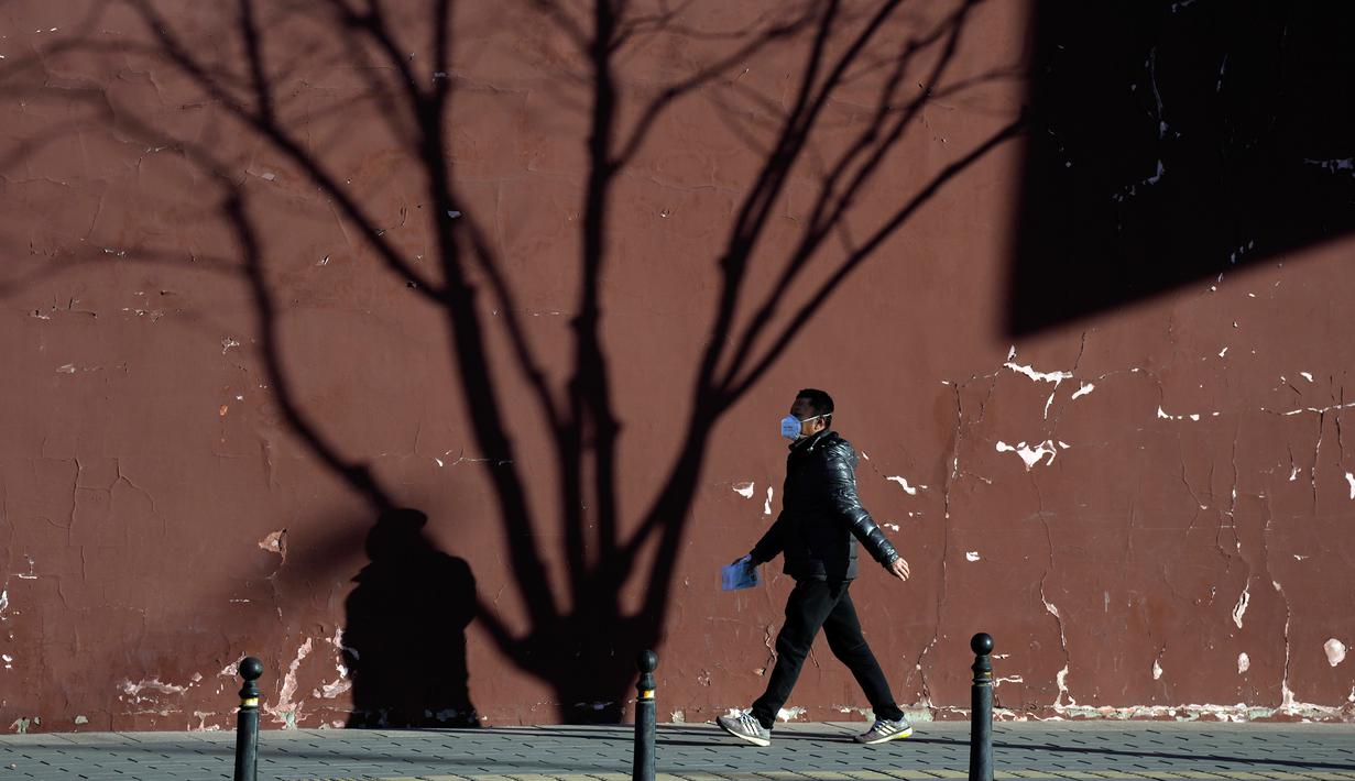 Seorang warga yang mengenakan masker berjalan dekat bayang-bayang pohon di Beijing, China, 27 Desember 2022. Perusahaan menyambut baik keputusan China untuk mengakhiri karantina bagi pelancong dari luar negeri sebagai langkah penting untuk menghidupkan kembali aktivitas bisnis yang merosot, sementara Jepang mengumumkan pembatasan pengunjung saat infeksi melonjak. (AP Photo/Ng Han Guan)