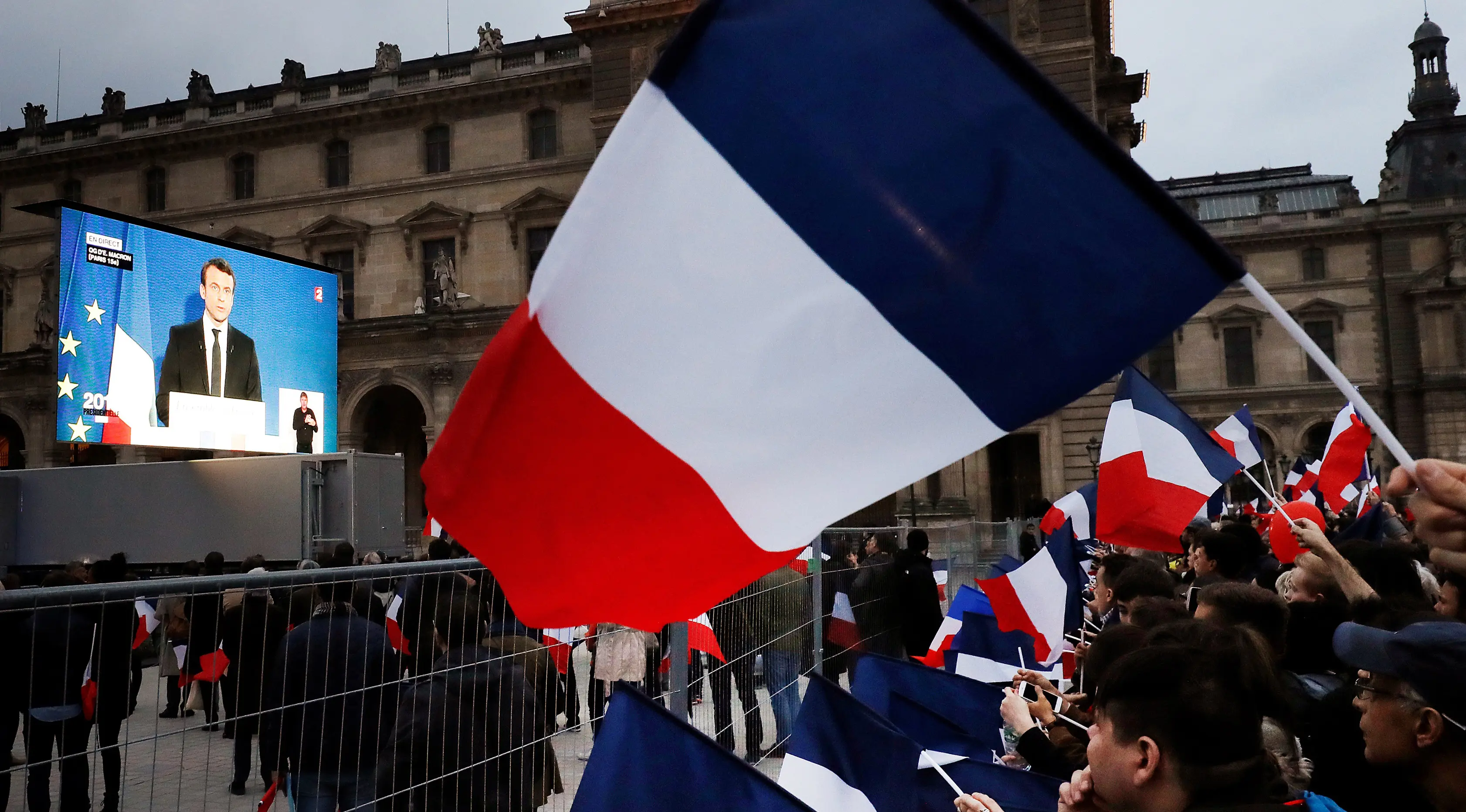 Para pendukung menonton pidato kemenangan Emmanuel Macron di luar museum Louvre, Paris, Minggu (7/5). Macron menjadi presiden Prancis setelah telak mengalahkan rivalnya Marine Le Pen dalam Pilpres Prancis putaran kedua. (Patrick KOVARIK / AFP)