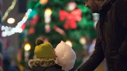 Seorang anak menyantap permen kapas di pasar Natal di St. Petersburg (20/12/2020). Wisatawan juga dapat mengunjungi konser dadakan, roti jahe, mainan, gua, dan wahana pasar malam. (Xinhua/Irina Motina)