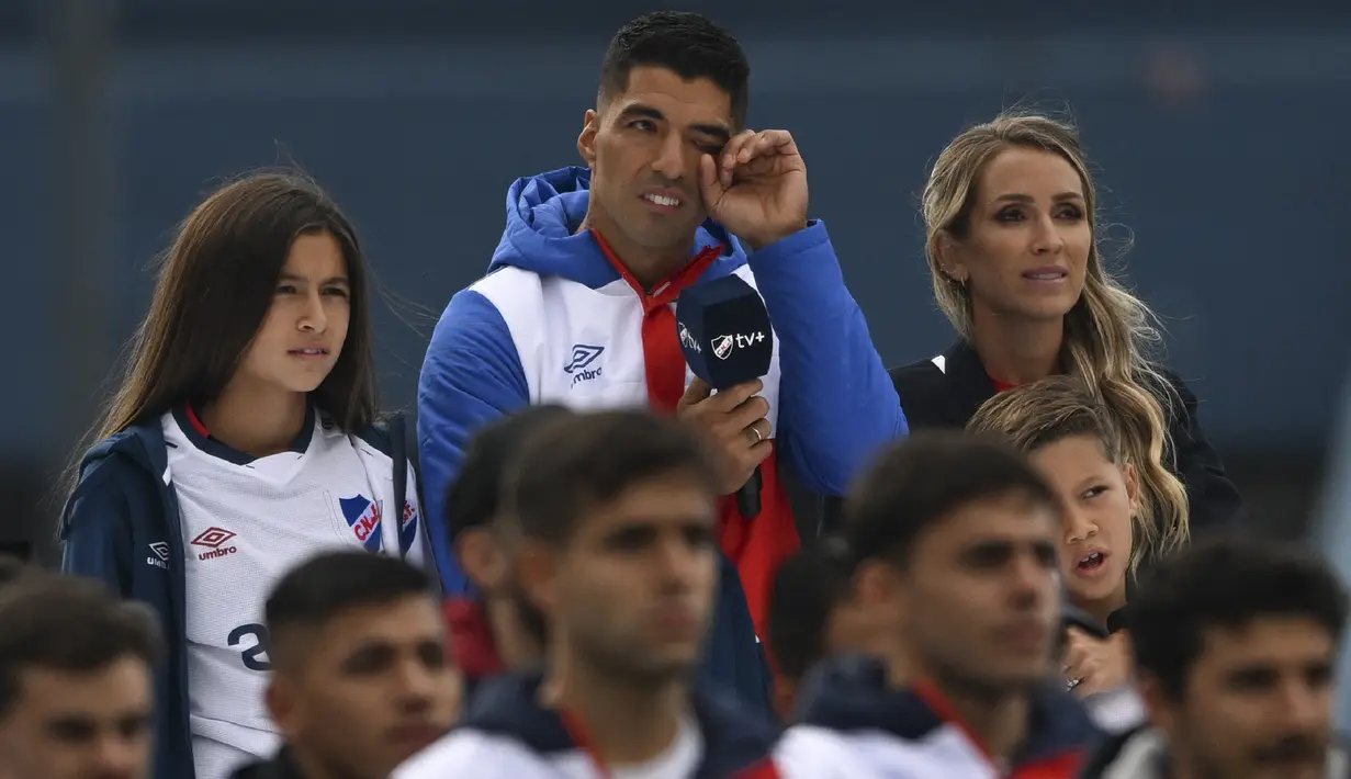 <p>Luis Suarez (tengah) menyeka matanya di antara putrinya Delfina (kiri) dan istrinya Sofia Balbi saat menonton video selama presentasinya sebagai pemain baru Nacional di Stadion Gran Parque Central, di Montevideo, pada 31 Juli, 2022. Luis Suarez kembali ke Uruguay untuk bergabung dengan Nacional, klub tempat ia memulai karirnya 17 tahun lalu sebagai salah satu striker terbaik di generasinya. (AFP/Pablo Porciuncula)</p>