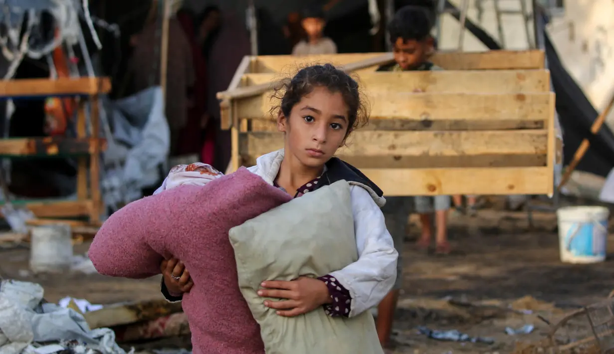 Seorang anak membawa barang-barang yang bisa diselamatkan setelah serangan udara Israel pada malam sebelumnya di kamp pengungsi Bureij di Jalur Gaza tengah pada 8 Oktober 2024. (Eyad BABA/AFP)