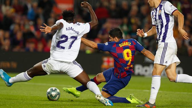 Striker Barcelona, Luis Suarez, menendang bola dibayangi pemain Real Valladolid, Mohammed Salisu dalam pertandingan pekan ke-11 La Liga di Camp Nou, Selasa (29/10/2019). Barcelonamenutup laga dengan kemenangan 5-1 lewat gol tambahan dari Lionel Messi dan Luis Suarez. (AP/Joan Monfort)