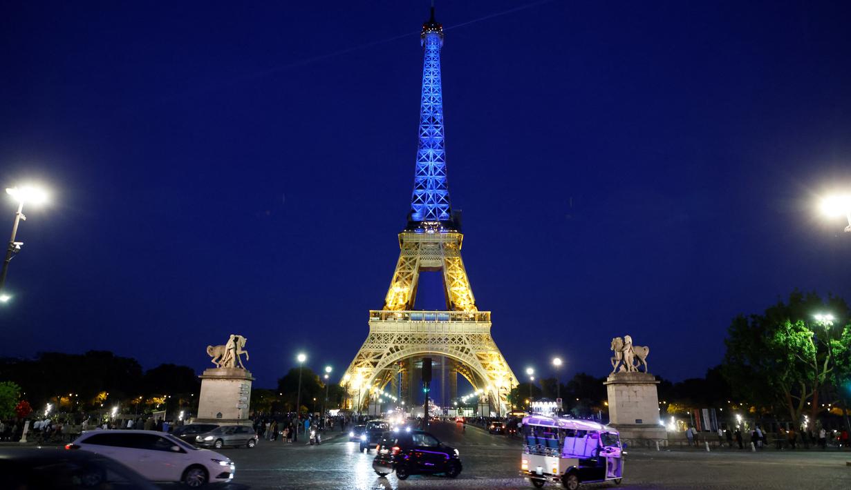 <p>Orang-orang&nbsp;melintas di dekat Menara Eiffel di Paris yang diterangi dengan warna bendera nasional Ukraina, pada 9 Mei 2022. Memperingati Hari Eropa, Menara Eiffel memproyeksikan bendera Ukraina sebagai solidaritas untuk rakyat Ukraina di tengah invasi Rusia. (Ludovic MARIN / AFP)</p>