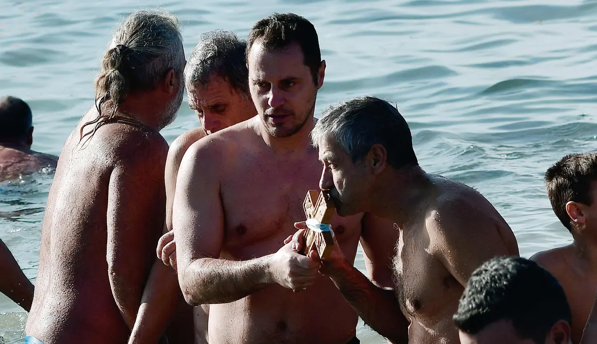 Seorang pria mencium sebuah salib kayu yang dilemparkan ke dalam air oleh seorang imam, di lepas pantai pinggiran pesisir Athena selama Hari Epiphany Orthodox, Yunani (6/1). (AFP Photo/Louisa Gouliamaki)