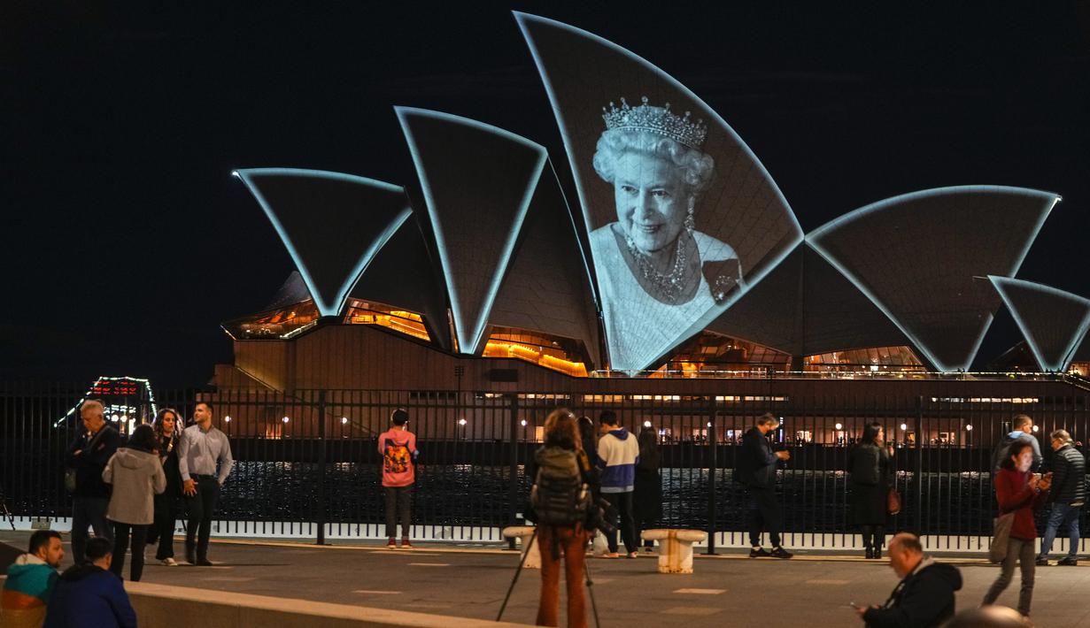 Orang-orang menyaksikan Sydney Opera House diterangi untuk menghormati Ratu Elizabeth II di Sydney, Australia, Jumat (9/9/2022). Sejumlah tempat pun turut menyampaikan duka cita atas meninggalnya sang ratu dengan berbagai cara, mulai dari mematikan lampu pencahayaan hingga mengibarkan bendera setengah tiang. (AP Photo/Mark Baker)
