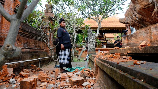 Pemuka agama memantau kerusakan pada bagian candi yang runtuh akibat gempa di Pura Lokanatha, Denpasar, Bali, Selasa (16/7/2019). Gempa Magnitudo 5,8  yang mengguncang Bali tidak menimbulkan korban jiwa, tapi sejumlah bangunan di beberapa kawasan mengalami kerusakan. (AP/Firdia Lisnawati)