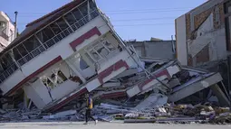 Seorang pria berjalan di depan bangunan yang hancur di Samandag, selatan Hatay pada 16 Februari 2023, sepuluh hari setelah gempa berkekuatan 7,8 melanda wilayah perbatasan Turki dan Suriah. Perserikatan Bangsa-Bangsa (PBB) meminta dana bantuan sebesar USD1 miliar atau Rp15,1 trilun untuk membantu para korban bencana gempa bumi di Turki yang menewaskan ribuan orang dan membuat jutaan lainnya sangat membutuhkan bantuan. (Photo by Yasin AKGUL / AFP)