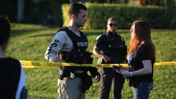 Seorang wanita bertanya kepada petugas kepolisian yang berjaga di lokasi penembakan massal sekolah menengah atas di Parkland, Florida, Rabu (14/2). Pelaku, Nikolaus Cruz (19), menembaki rekannya sesama siswa menggunakan senapan serbu AR-15. (AP PHOTO)