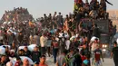 Orang-orang naik ke atas dan bergelantungan di atas truk yang mengangkut mereka, sementara yang lain berjalan sambil membawa karung-karung tepung di sepanjang jalan al-Rashid di Jabalia Barat pada 17 Juni 2025. (BASHAR TALEB/AFP)