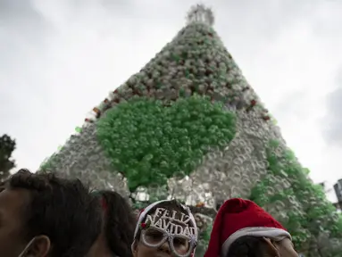 Anak-anak yang mengenakan topi Sinterklas menghadiri upacara penyalaan pohon Natal yang terbuat dari botol plastik daur ulang di Caracas, Venezuela, Selasa (13/12/2022). Pohon Natal yang dibuat dari sekitar 15.000 botol plastik daur ulang ini diinisiasi oleh organisasi nirlaba dan non-pemerintah Oko Spire dan kolaborator. (Yuri CORTEZ / AFP)