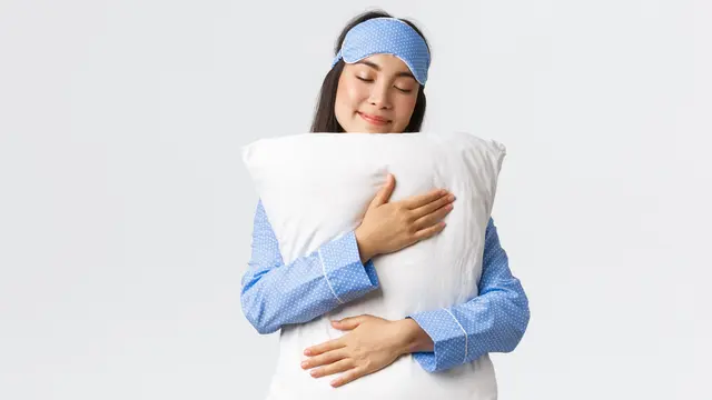 Seorang perempuan dengan piyama memeluk sebuah bantal (Foto Dok: Freepik/benzoix)