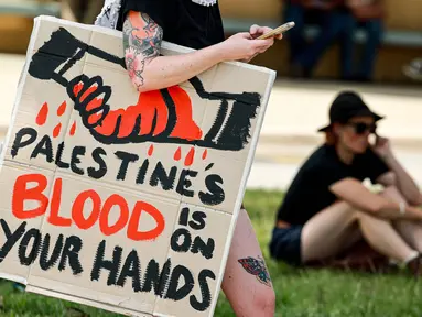 Seorang demonstran dengan membawa papan tanda bergabung dengan yang lain di luar gedung Parlemen menjelang pertemuan antara Perdana Menteri Australia Anthony Albanese dan Presiden Israel Isaac Herzog di Canberra pada Rabu 11 Februari 2026. Kunjungan resmi Presiden Israel, Isaac Herzog, ke Australia memicu gelombang unjuk rasa pro-Palestina di berbagai kota besar seperti Sydney, Melbourne, dan Canberra. (DAVID GRAY/AFP)