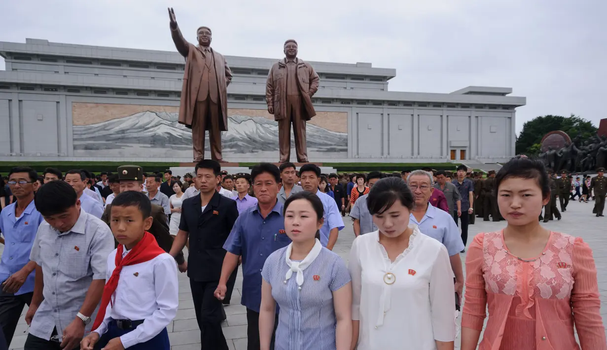 Warga Pyongyang berjalan di depan patung pemimpin Korea Utara Kim Il Sung (kiri) dan Kim Jong Il (kanan), setelah meletakkan bunga untuk menandai peringatan 24 tahun kematian Kim Il Sung, di bukit Mansu, Minggu (8/7). (AFP/KIM Won-Jin)