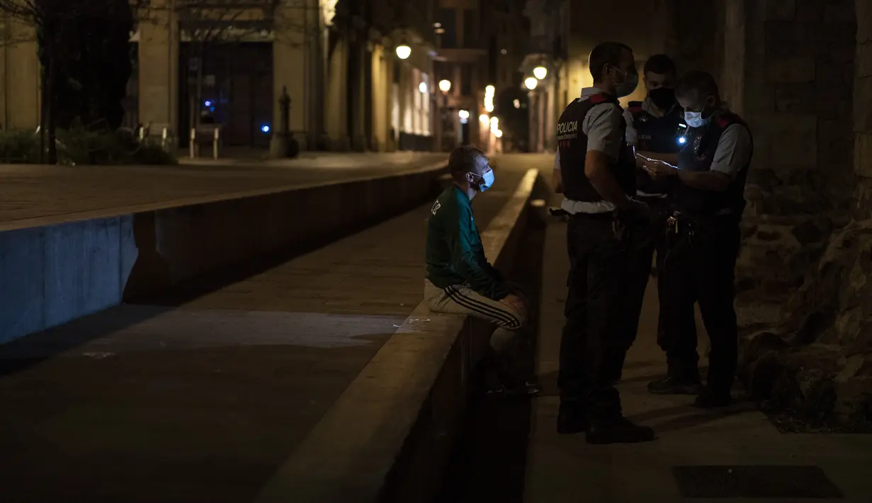 Seorang pria ditahan oleh Mossos d'Escuadra, kepolisian regional Catalonia, setelah jam malam di Barcelona pada 1 November 2020. Pemerintah Spanyol menetapkan pembatasan gerak atau jam malam yang berlaku pukul 22.00 untuk mengendalikan lonjakan kasus Covid-19. (AP Photo/Emilio Morenatti)