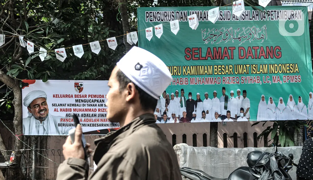 Anggota FPI melintasi poster penyambutan Habib Rizieq di Jalan Petamburan III, Jakarta, Senin (9/11/2020).  Habib Rizieq dijadwalkan juga akan mengunjungi pengajian di Tebet, dan meletakkan batu pertama prmbangunan pesantren di Megamendung, Bogor. (merdeka.com/Iqbal S. Nugroho)