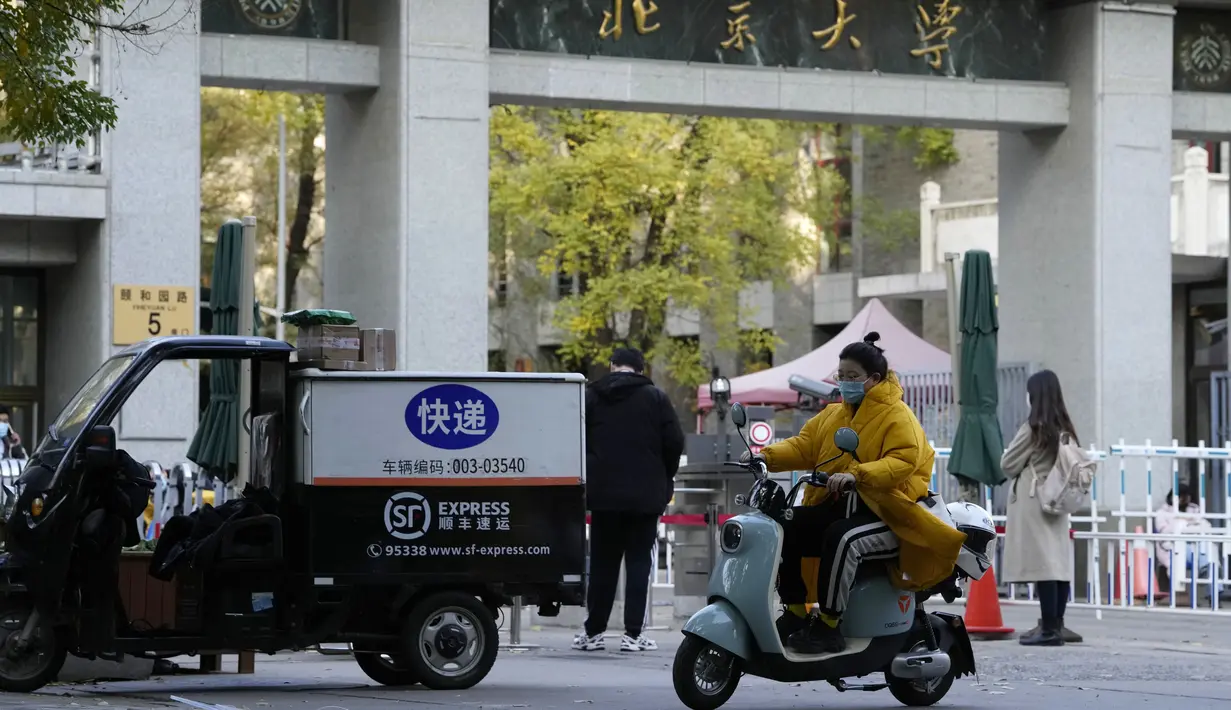 Seorang perempuan yang mengenakan masker melewati pintu masuk Universitas Peking di Beijing, Rabu (16/11/2022). Pihak berwenang China mengunci Universitas Peking setelah temuan satu kasus virus Corona Covid-19 di area kampus. (AP Photo/Ng Han Guan)