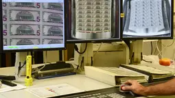 Pekerja memeriksa pencetakan otomatis di Biro Pengukiran dan Percetakan AS di Washington DC, Jumat (20/7). Pembuatan dolar AS terdiri dari perancangan, ukiran, siderografi, pembuatan lempengan, cetak offset, inspeksi dan pengemasan. (Eva HAMBACH/AFP)