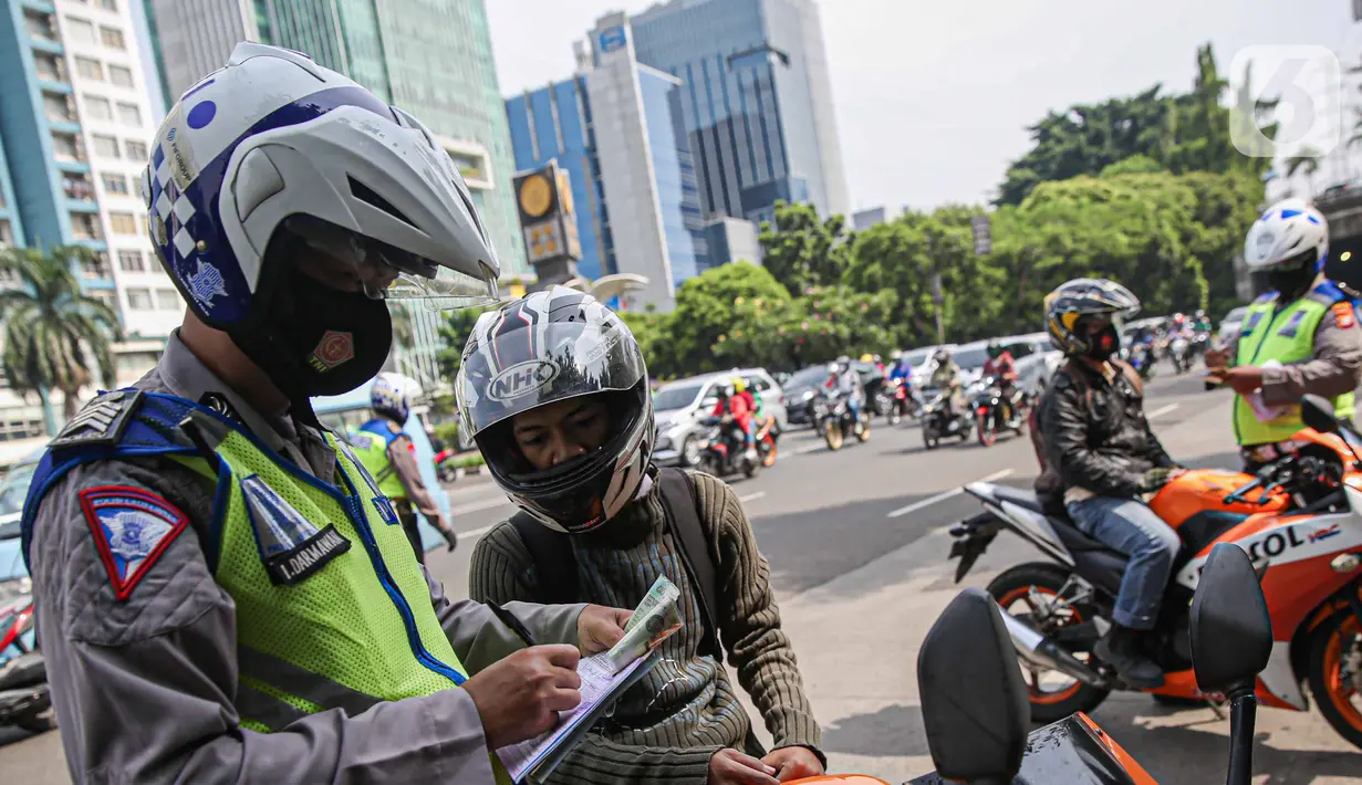 Petugas kepolisian lalu lintas saat menilang pengendara motor saat Operasi Zebra Jaya 2020 di kawasan Cawang, Jakarta, Senin (26/10/2020). Operasi Zebra Jaya dilaksanakan pada 26 Oktober-8 November 2020 untuk menekan jumlah pelanggaran lalu lintas. (Liputan6.com/Faizal Fanani)