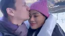 Tidak hanya membagikan momen harmonis, Titi Kamal juga membagikan momen romantis. Christian Sugino mencium kening sang istri saat berada di kereta gantung. [Instagram/titi_kamall]