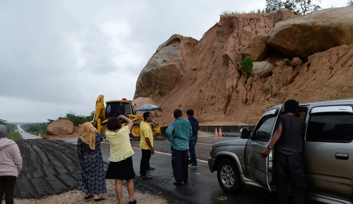Orang-orang melihat batu-batu besar di jalan raya menuju bandara Narathiwat menyusul tanah longsor setelah hujan lebat di Thailand selatan (25/11/2019). Wilayah selatan Thailand akan memasuki musim hujan lebat tiga bulan dari November hingga Januari. (AFP/Madaree Tohlala)