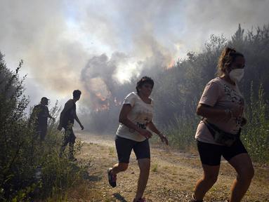 Orang-orang berlari untuk menyelamatkan diri dari api kebakaran hutan di dekat desa Melon, Spanyol barat laut, pada 17 Agustus 2025. (MIGUEL RIOPA/AFP)