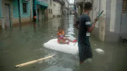 Seorang pria membantu gadis kecil mengapung di atas styrofoam untuk melewati banjir di Hanava, Kuba, Minggu (10/9). Badai irma yang melanda pantai timur Perairan Kuba pada Jumat waktu setempat menyebabkan sebagian kota terendam banjir. (AP/Ramon Espinosa)