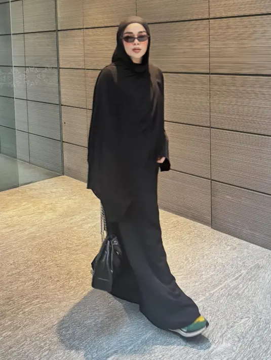 Sivia mengenakan pashimina hitam panjang polos serasi dengan abaya hitam polosnya. Dipadukan kacamata hitam sambi membawa tas hitamnya. Mengenakan sepatu sneakers hijau. [@siviazizah]