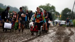 Penonton Festival Glastonbury membawa barang-barang mereka melewati jalanan yang banjir dan berlumpur saat tiba di Worthy Farm, Somerset, Inggris, (22/6). Di gelaran ke-34 kali ini akan menghadirkan musisi-musisi hebat dunia. (REUTERS / Stoyan  Nenov)