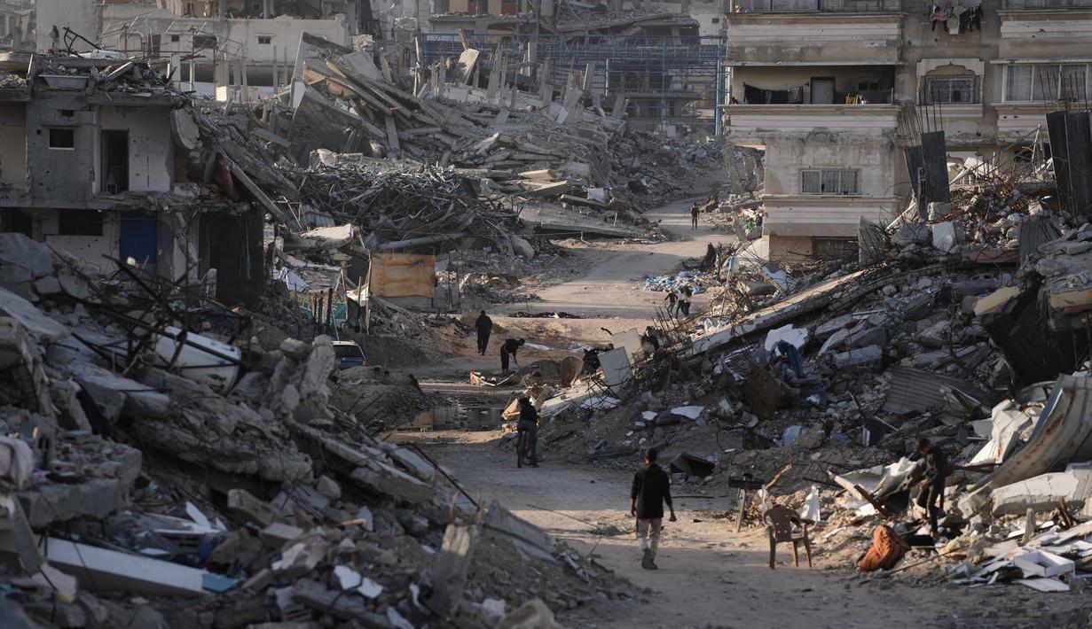 Jabalia, wilayah yang menjadi salah satu kamp pengungsi terbesar dan terpadat di Gaza, mengalami kehancuran infrastruktur yang parah. Tampak dalam foto, orang-orang berjalan di antara bangunan-bangunan yang hancur di Jabalia, di bagian utara Jalur Gaza, Minggu 7 Desember 2025. (AP Photo/Jehad Alshrafi)