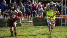Dua tim bersaing sambil menggendong istri mereka dalam North American Wife Carrying Championship di Sunday River Resort di Newry, Maine, pada 8 Oktober 2022. Secara aturan, satu tim harus terdiri dari pria dan wanita yang telah berumur 21 tahun ke atas. (Joseph Prezioso / AFP)