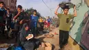 Seorang anak laki-laki Palestina berjalan melewati orang-orang yang sedang membuat roti tidak beragi di lokasi penampungan bagi keluarga pengungsi, Jalur Gaza Selatan, 27 Oktober 2023. (SAID KHATIB/AFP)