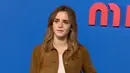 Emma Watson hadir mengenakan long outer coklat dipadukan inner mini dress soft pink. Ia membawa hand mini bag hitam senada dengan warna heels strapnya. [Dok. @wwd]