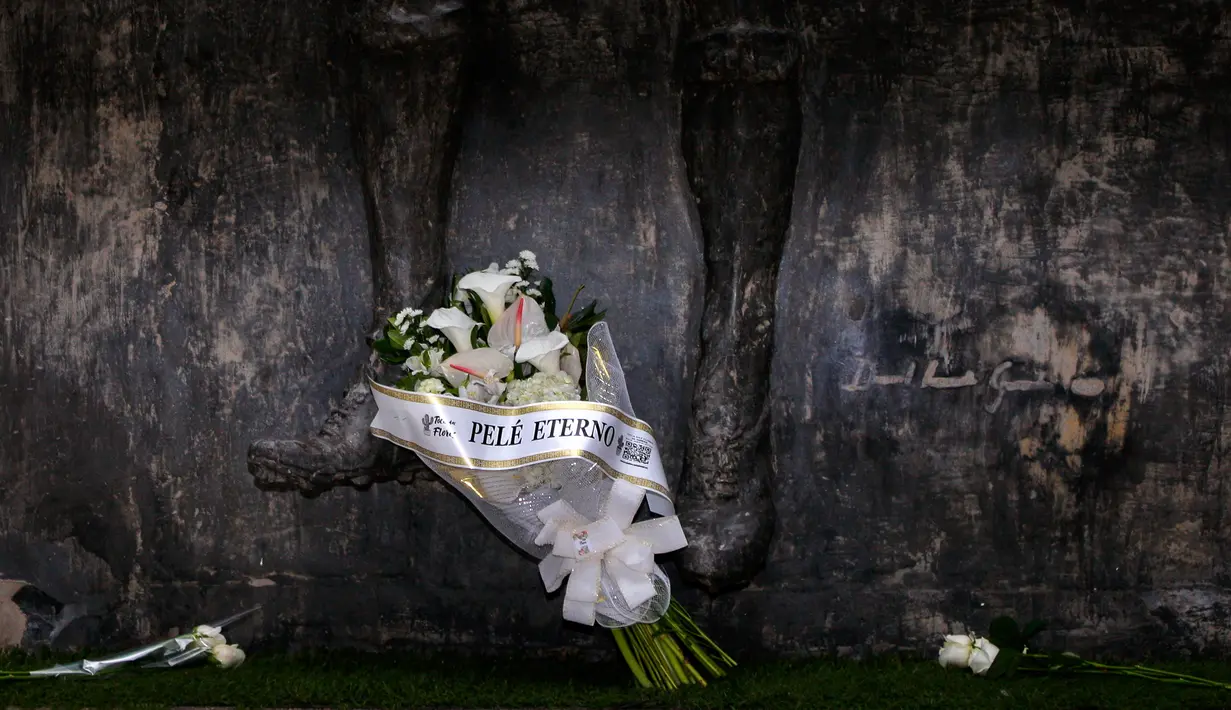Penggemar mendiang bintang sepak bola Brazil Pele meninggalkan karangan bunga bertuliskan "Pele Abadi" di kaki patungnya di Stadion Vila Belmiro, markas klub sepak bola Santos FC, di Santos, Brazil, 29 Desember 2022. Pele yang menghabiskan sebagian besar kariernya bersama Santos FC meninggal dunia di Sao Paulo. (AP Photo/Fabricio Costa)