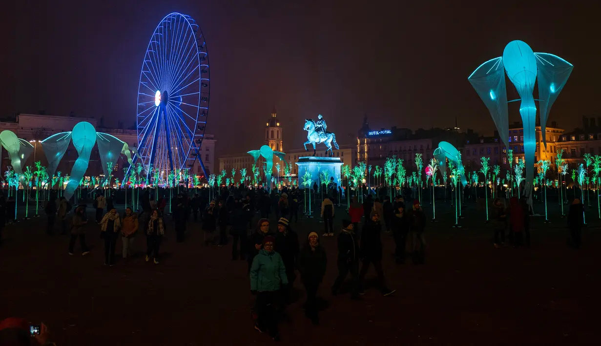 Orang-orang berjalan dekat instalasi lampu, Patung Louis XIV yang diterangi cahaya lampu dan kincir ria di Bellecour Place selama Festival of Lights (Fete des Lumieres) di kota Lyon, Prancis, Kamis (5/12/2019). Festival ini berlangsung, bertepatan dengan musim liburan Natal. (ROMAIN LAFABREGUE