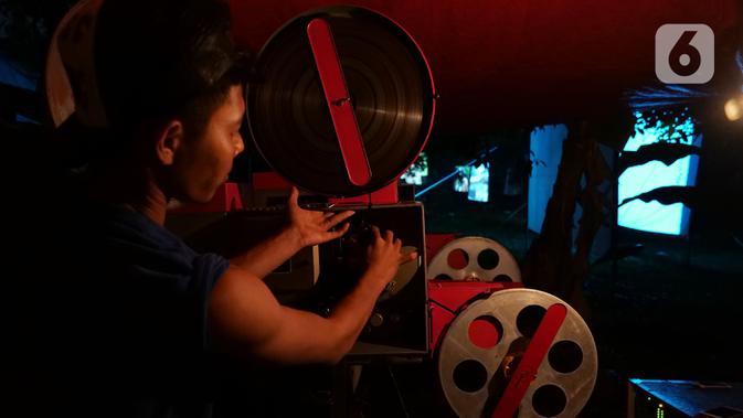 Teknisi memasukan film ke  proyektor film layar tancap di kawasan Sawangan, Depok, Jawa Barat, Sabtu (11/7/2020). Layar tancap atau bioskop terbuka menjadi alternatif bagi warga untuk menikmati film di tengah penerapan new normal di kawasan Jabodetabek. (Liputan6.com/Herman Zakharia)