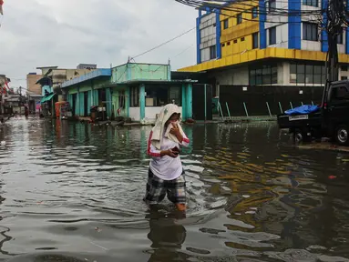 Warga melintasi banjir rob yang terjadi di kawasan Muara Baru, Jakarta Utara, Selasa (14/1/2025). (Liputan6.com/Angga Yuniar)