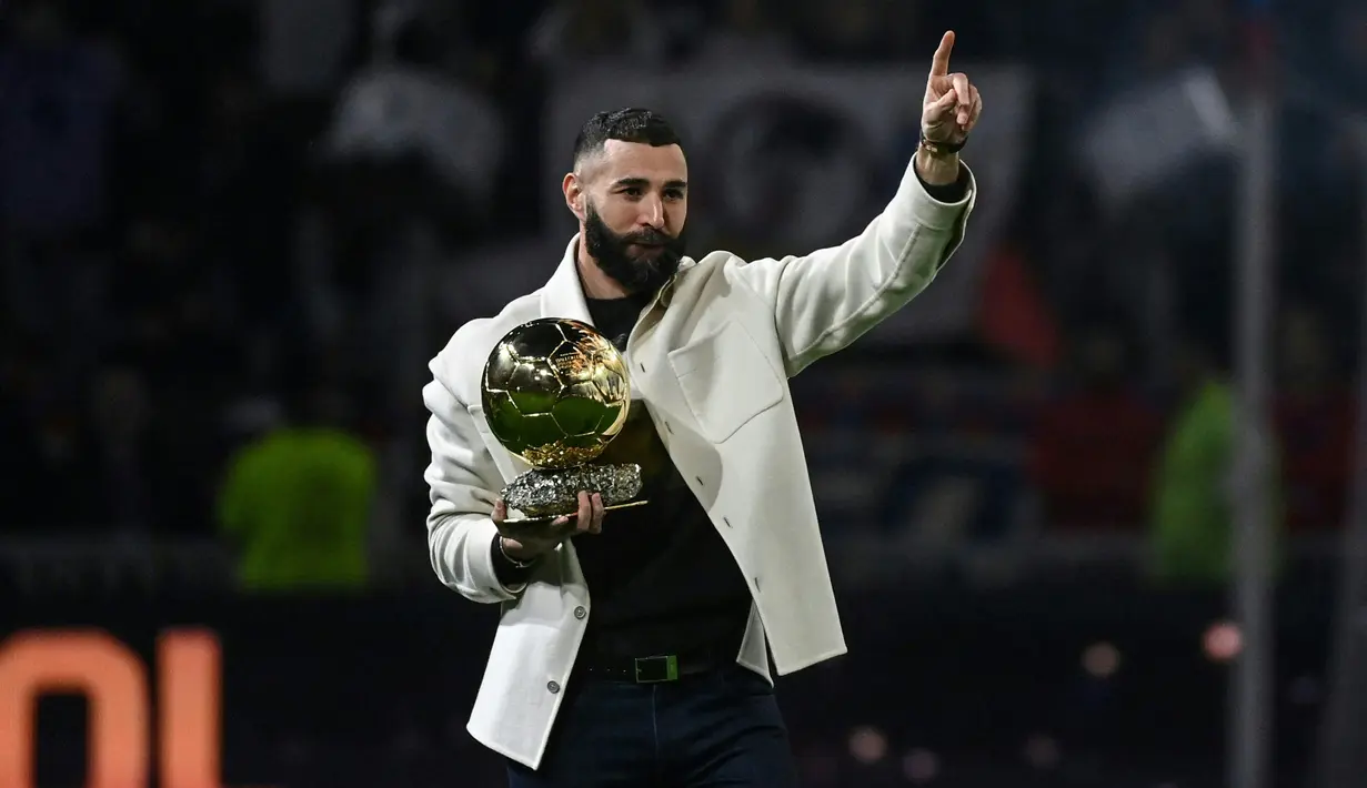 Pemain Real Madrid Karim Benzema berpose di lapangan dengan trofi Ballon d'Or miliknya pada paruh waktu pertandingan sepak bola L1 Prancis antara Olympique Lyonnais (OL) dan OGC Nice di Stadion Groupama, Decines-Charpieu, Prancis, 11 November 2022. Ia memperkuat Lyon senior sejak 2005 silam. (OLIVIER CHASSIGNOLE/AFP)