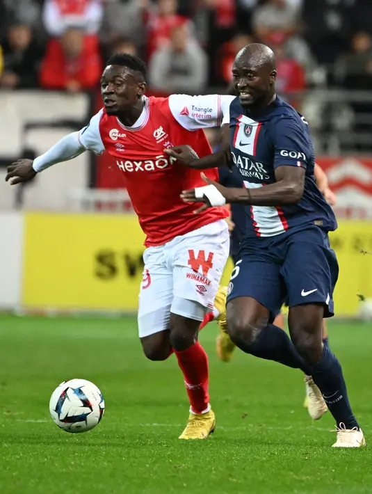 Penyerang Reims, Folarin Balogun (kiri) berebut bola dengan gelandang Paris Saint-Germain (PSG) Danilo Pereira dalam pertandingan pekan ke-10 Liga Prancis di Stade Auguste-Delaune II, Minggu (9/10/2022) dini hari WIB. Mampu menguasai bola dengan baik, PSG terus berusaha menciptakan peluang, namun Reims tampak sudah cukup siap untuk menahannya. (DENIS CHARLET / AFP)
